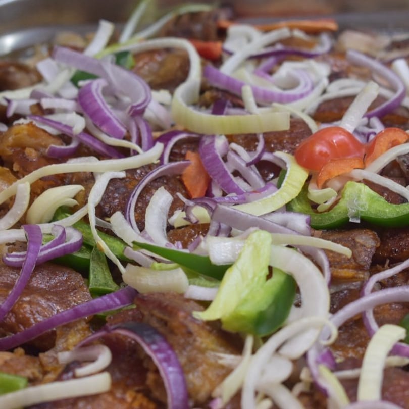 Close-up of John's Fried Chicken pieces topped with sliced red onions, white onions, and green peppers.