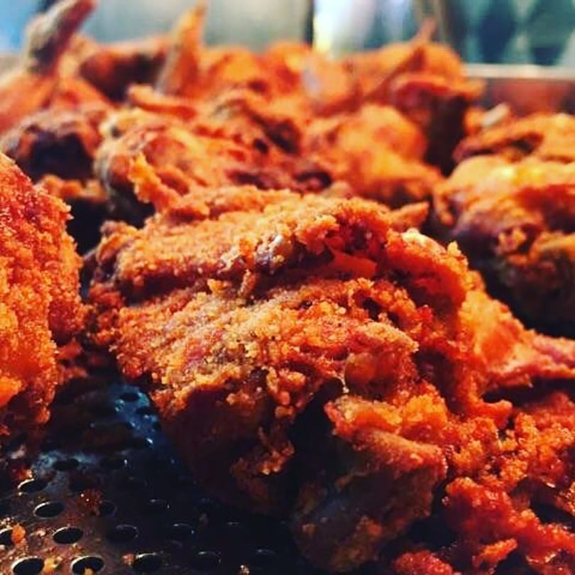 Close-up of crispy, golden-brown fried chicken pieces from John's Fried Chicken on a metal grate.