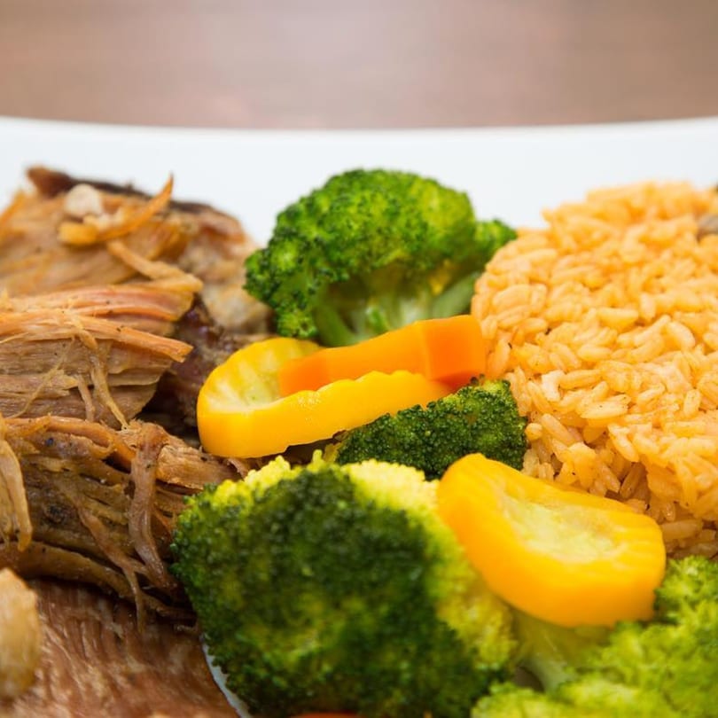 Shredded meat, rice, broccoli, and yellow bell peppers on a white plate.